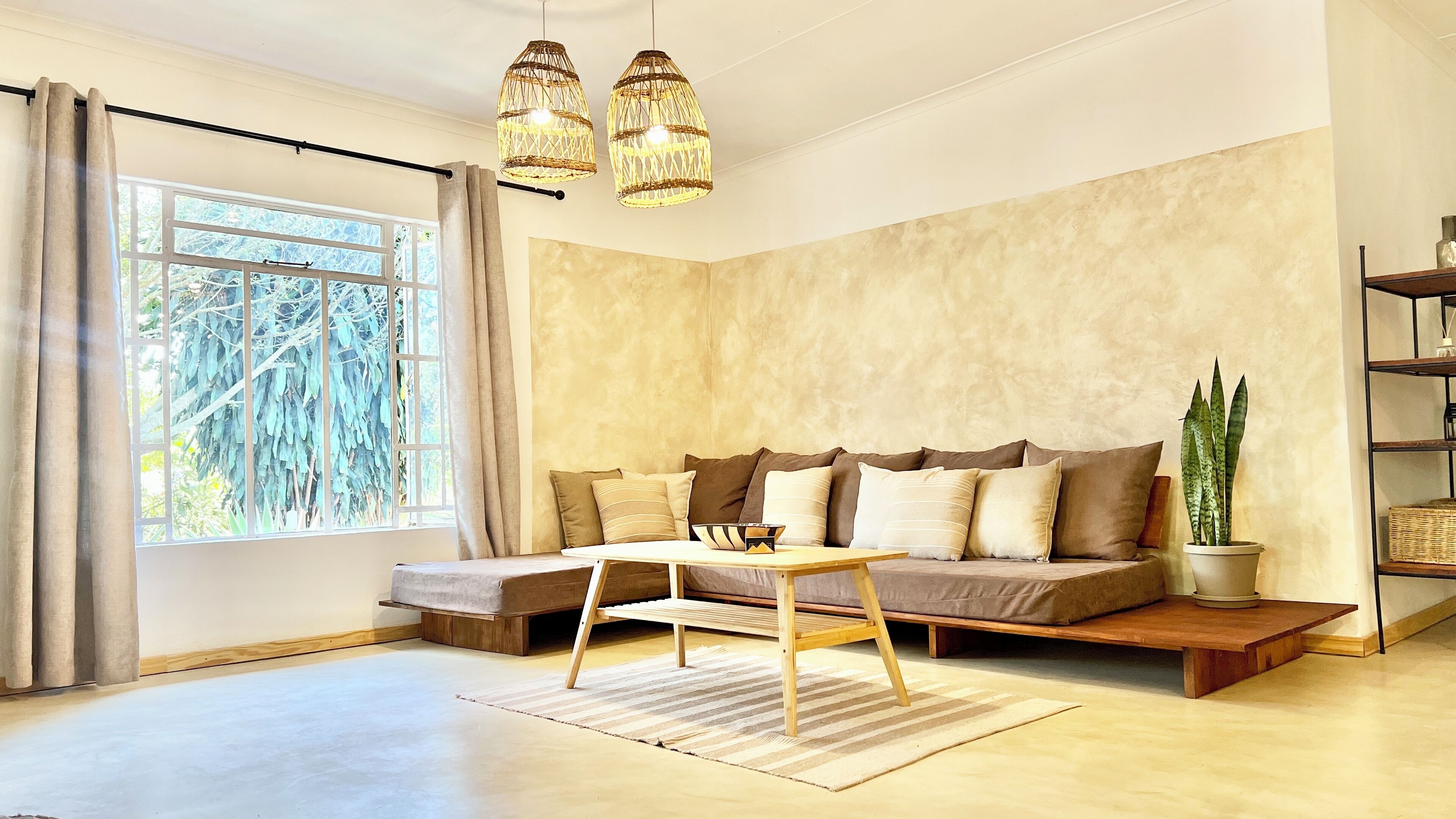 En moderne stue med sofa, sofabord og et stort vindue med gardiner.