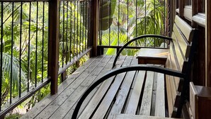 A wooden deck with a bench, surrounded by metal railings, overlooking a lush garden with various trees and plants. - LoerieRoep (Mbombela)