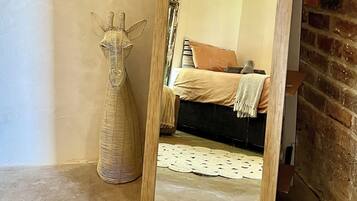 A mirror reflecting a room with a bed, a hanging light fixture, and a wicker vase.