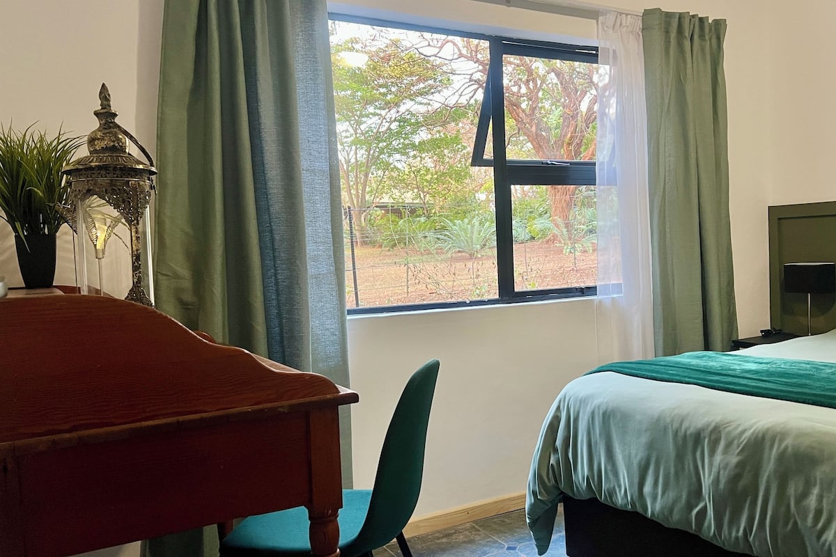 A hotel room with a bed, a desk, a chair, a nightstand, and a window with curtains.