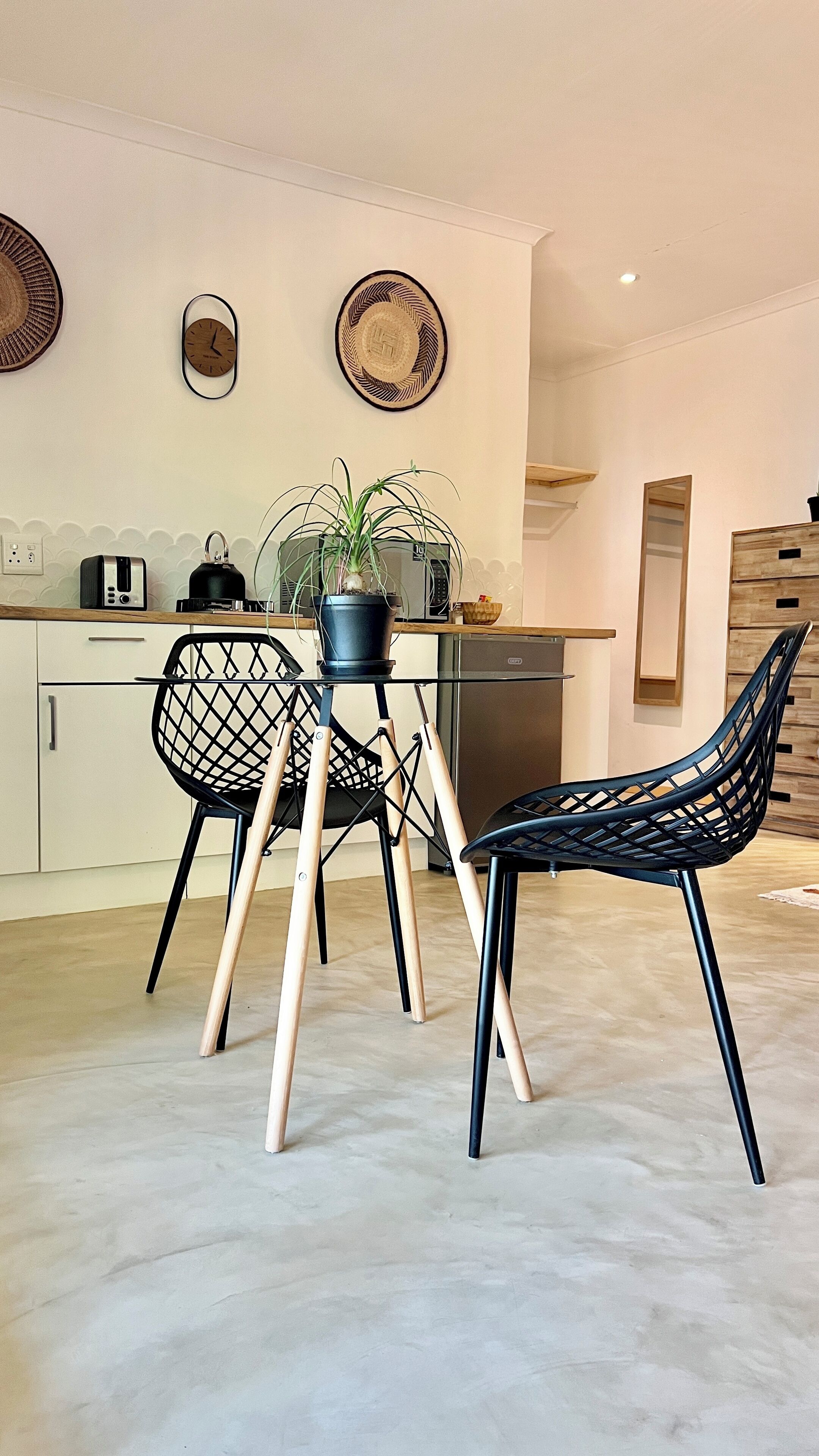 Una cocina moderna con una mesa de comedor, dos sillas, una planta en maceta y un microondas.