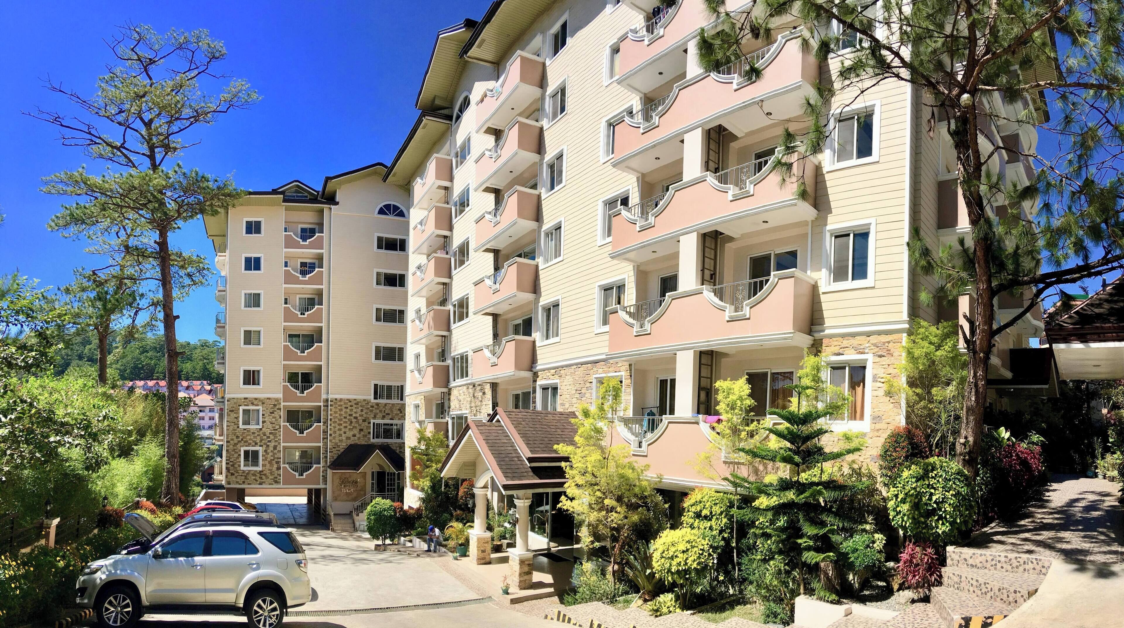 Un immeuble résidentiel à plusieurs étages, doté de balcons, d’une entrée couverte et entouré de verdure.