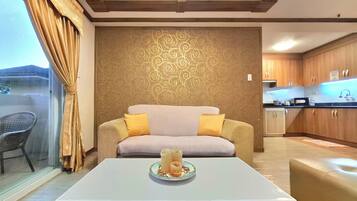 A modern living room with a sofa, a coffee table with a decorative item, a patterned wall, and a kitchen area visible through an open door.