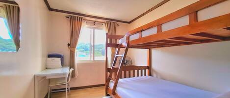 A room with a bunk bed, a desk, and a window with curtains.