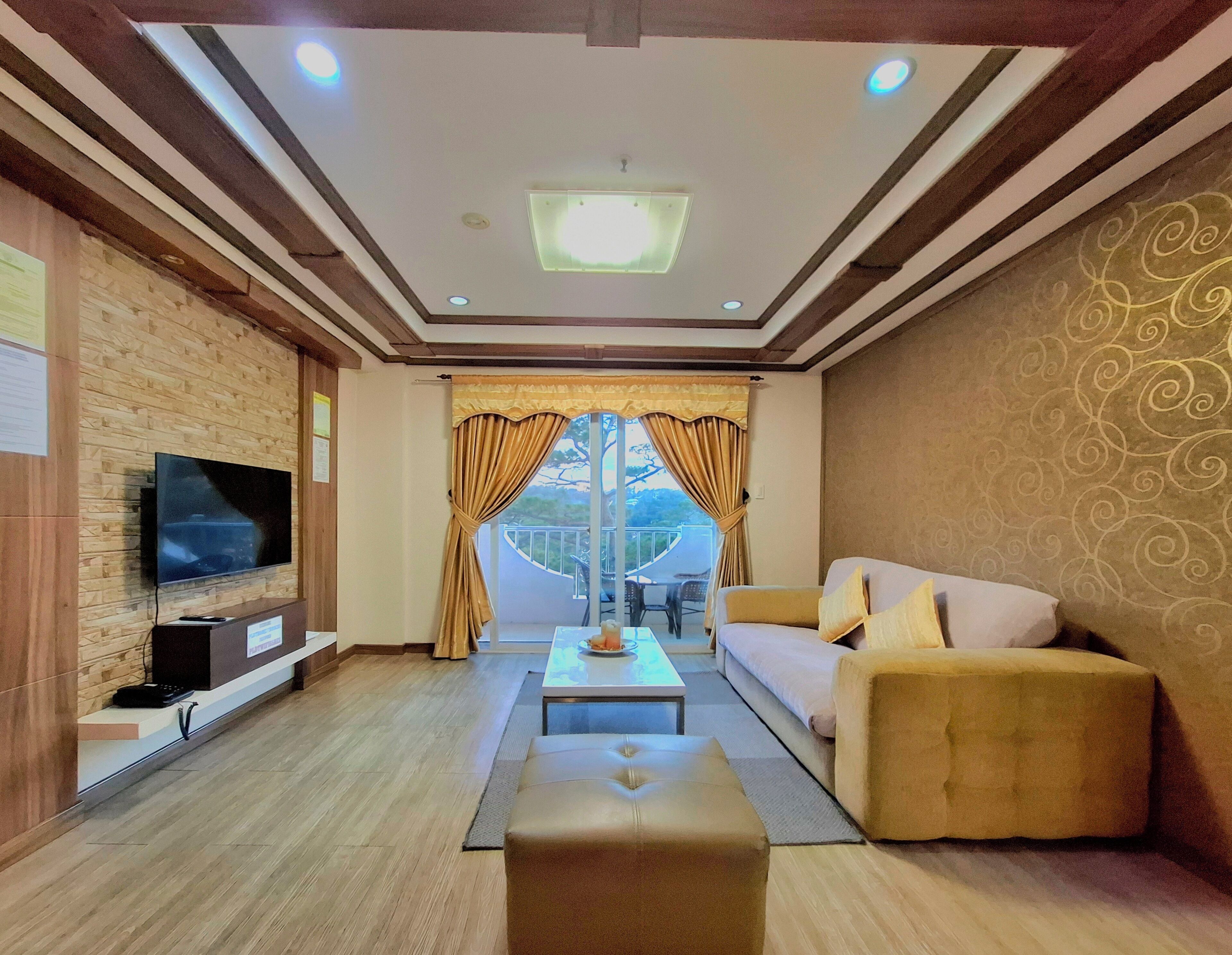 Een moderne woonkamer met een flatscreen televisie, een bank, een salontafel en uitzicht op de natuur door grote ramen.
