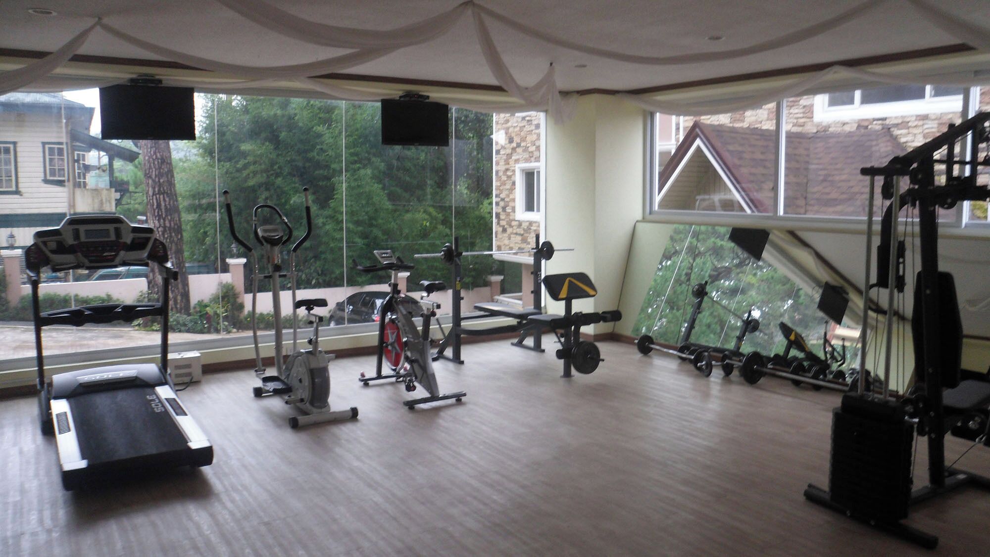 A gym with cardio equipment, weight machines, and a large window offering a view of the outdoors.