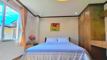 A bedroom with a bed, a nightstand with a vase of flowers, a wooden wardrobe, and a window with curtains.