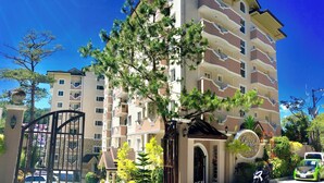 A multi-story hotel with a gated entrance, surrounded by trees and a clear blue sky. - Prestige Vacation Apartments - Bonbel Condominium (Baguio)