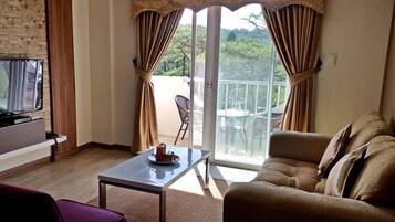 A living room with a sofa, a coffee table, a TV, and a balcony with curtains.