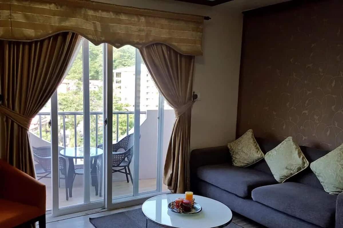 Een woonkamer met een bank, een bijzettafeltje met een kaars, en een balkon met stoelen en een tafel.