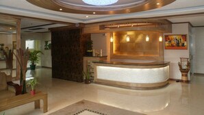 A lobby with a reception desk, a chandelier, and a painting on the wall. - Prestige Vacation Apartments - Bonbel Condominium (Baguio)