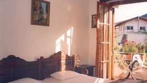 A bedroom with a wooden bed, a window with a view of a house and garden, and a painting on the wall. - Katerina Hotel (Nafplio)