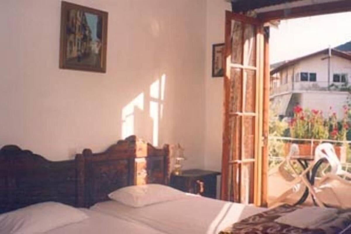 Une chambre avec un lit en bois, une fenêtre donnant sur une maison et un jardin, et un tableau accroché au mur.