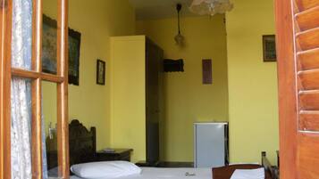 A room with two beds, a wooden headboard, a small desk, a refrigerator, and a hanging light fixture.