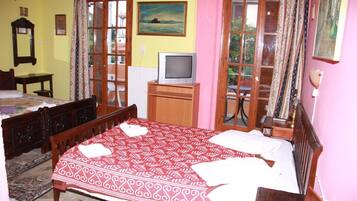 A bedroom with a bed, a television, a desk, and a window with curtains.