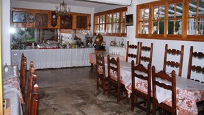 A dining area with wooden chairs and a table, a kitchen area with cabinets and a counter, and a window with wooden frames. - Katerina Hotel (Nafplio)