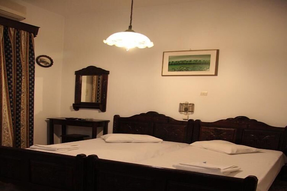 A double bed with a wooden frame, a bedside table, a mirror, a lamp, and a framed picture on the wall.