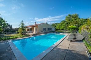 Una piscina rectangular con borde de azulejos, rodeada por un suelo de concreto y una cerca de metal.