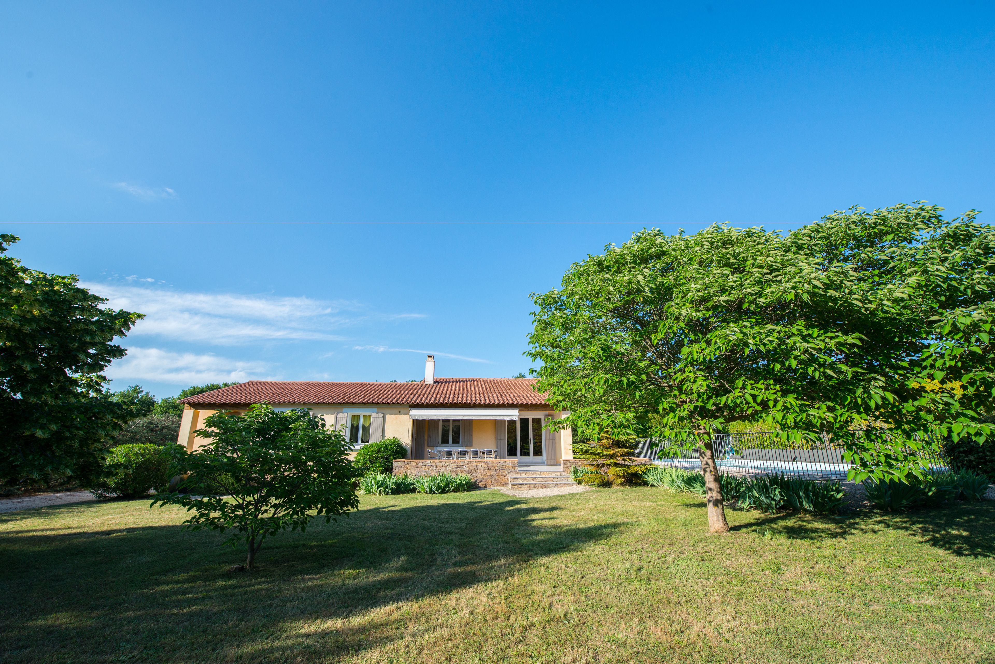 Une maison avec un toit rouge, un porche à l’avant et une pelouse bien entretenue.