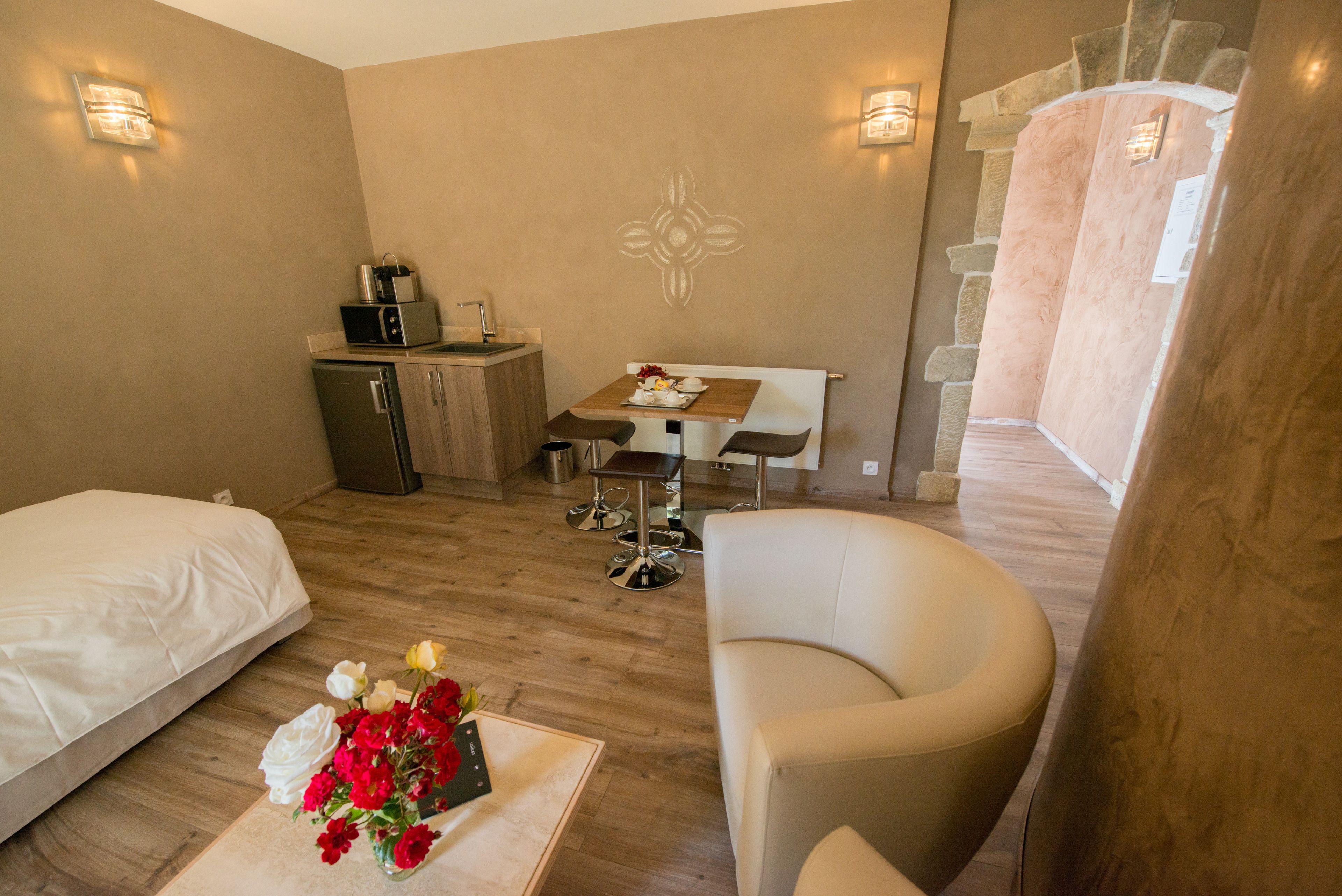 Une chambre d’hôtel comprenant un lit, un canapé, un bureau avec une chaise, une petite kitchenette et un élément décoratif mural.
