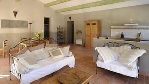 A spacious living area with a high ceiling and exposed beams, a dining area with a table and chairs, and a kitchenette with a stove. - La Ferme Du Gros Noyer (Malaucene)