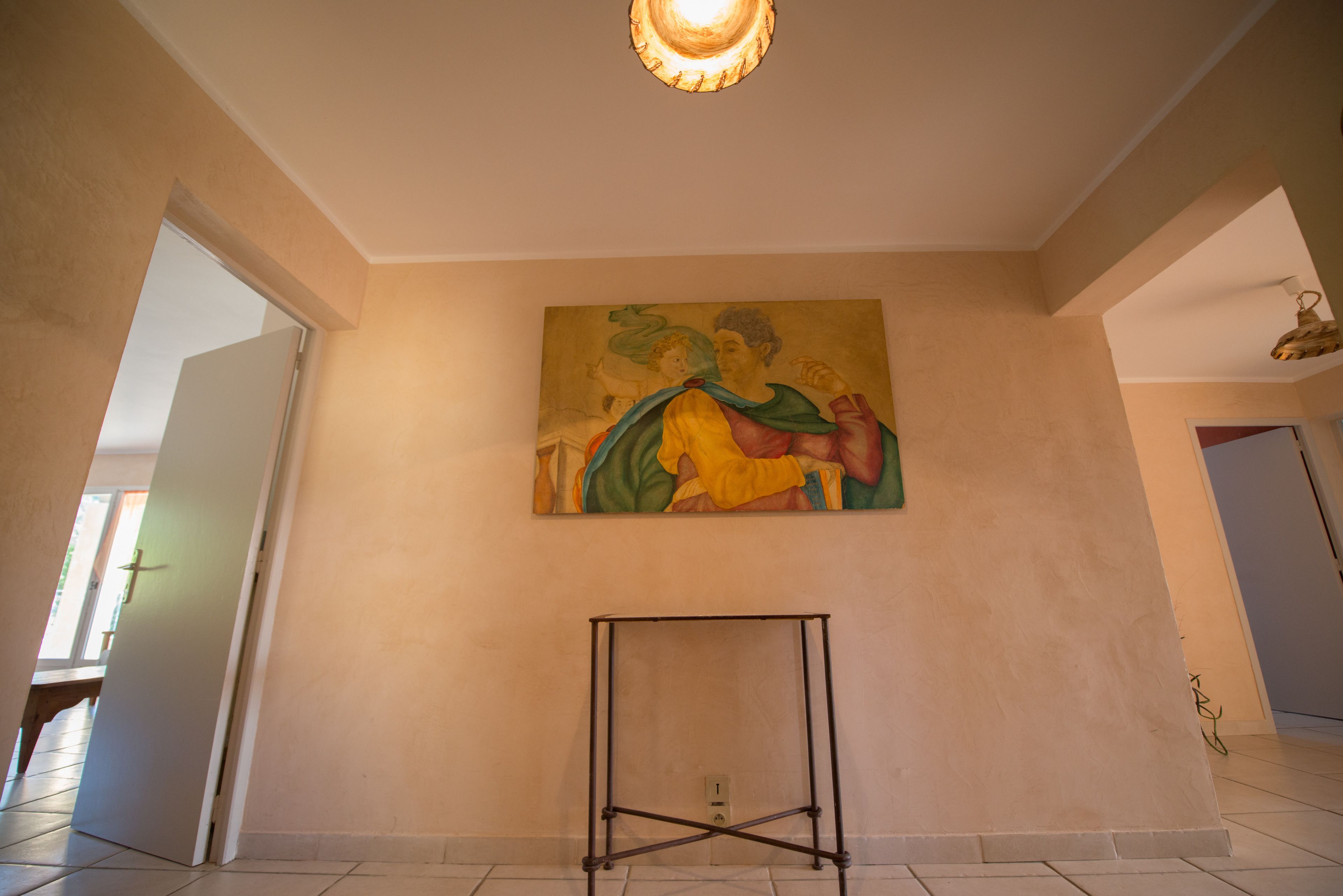 A room with a large painting on the wall, a standing lamp, and a door leading to another room.
