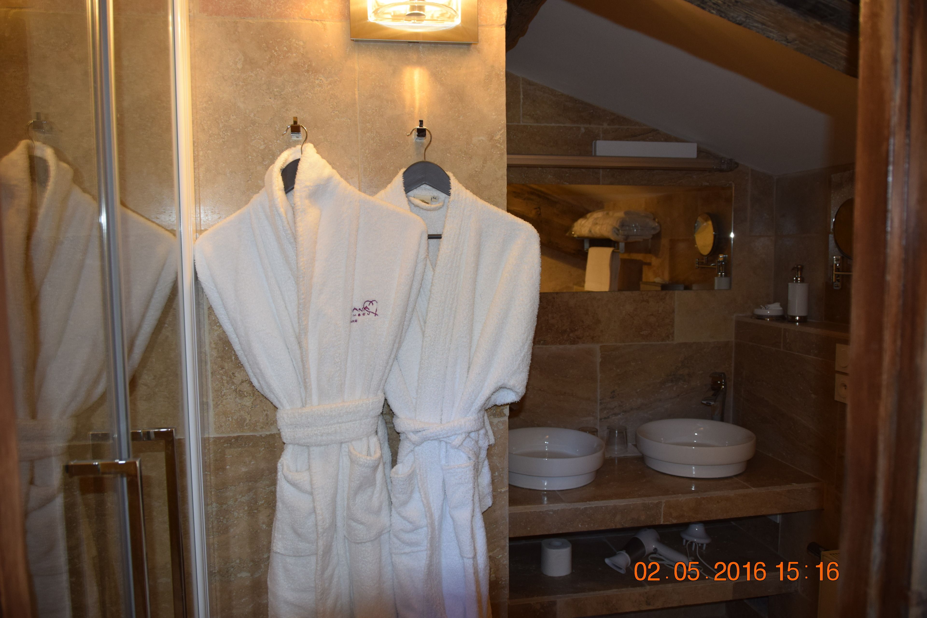 A bathroom with two white bathrobes hanging on a rack, a round sink, and a mirror above the sink.