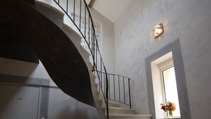 A spiral staircase with a modern design, a small window with a flower arrangement, and a light fixture on the wall. - La Ferme Du Gros Noyer (Malaucene)