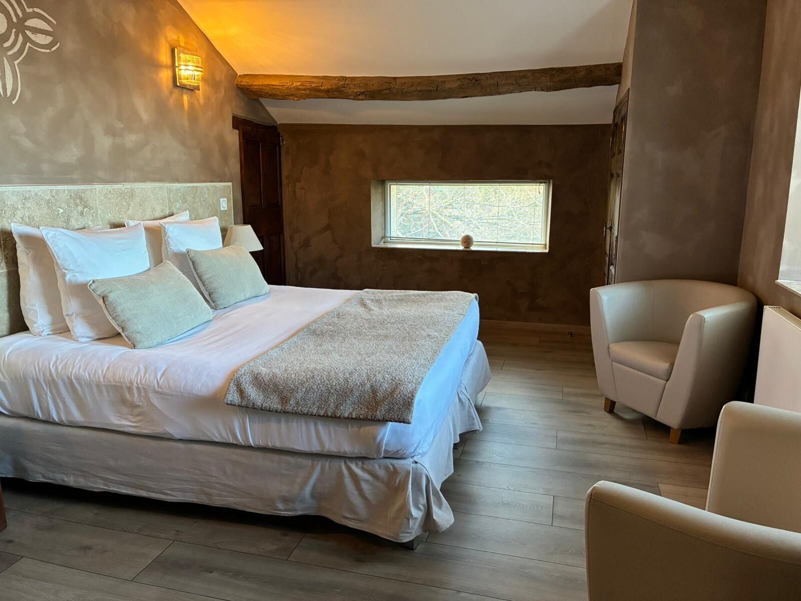 A bedroom with a large bed, a chair, and a window.