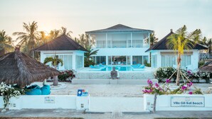Une villa à deux étages dotée d’une piscine, de palmiers et offrant une vue sur la plage.