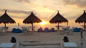 Une plage aménagée avec des parasols en chaume, des chaises blanches et des fauteuils en forme de poire.