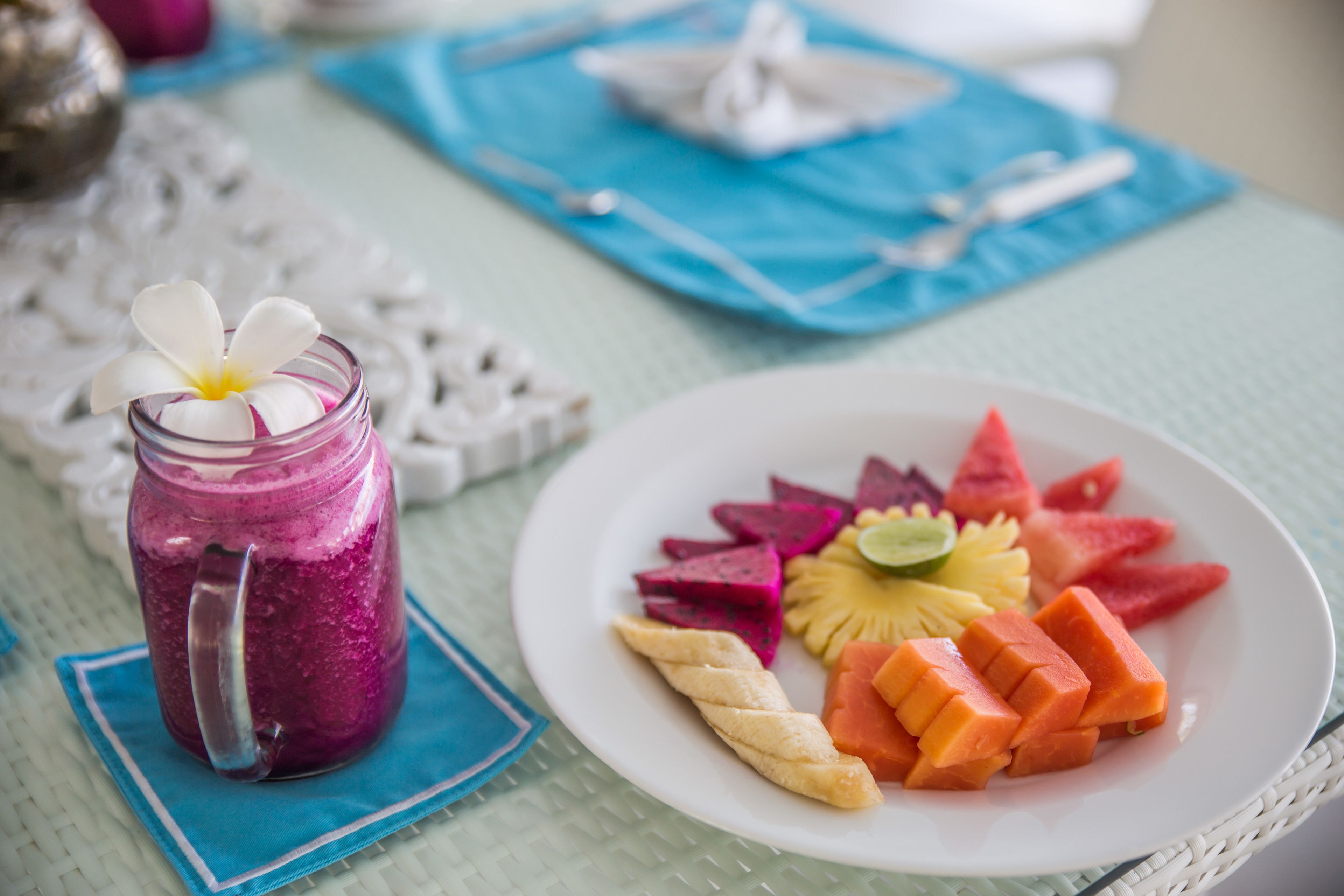 A table with a plate of fruit, a glass of smoothie, and a napkin.