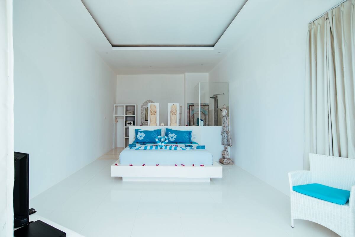 Un dormitorio moderno con una cama, una silla blanca y una televisión.