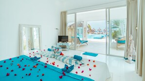 Une chambre spacieuse avec un grand lit, une télévision et une vue sur la piscine et la plage.