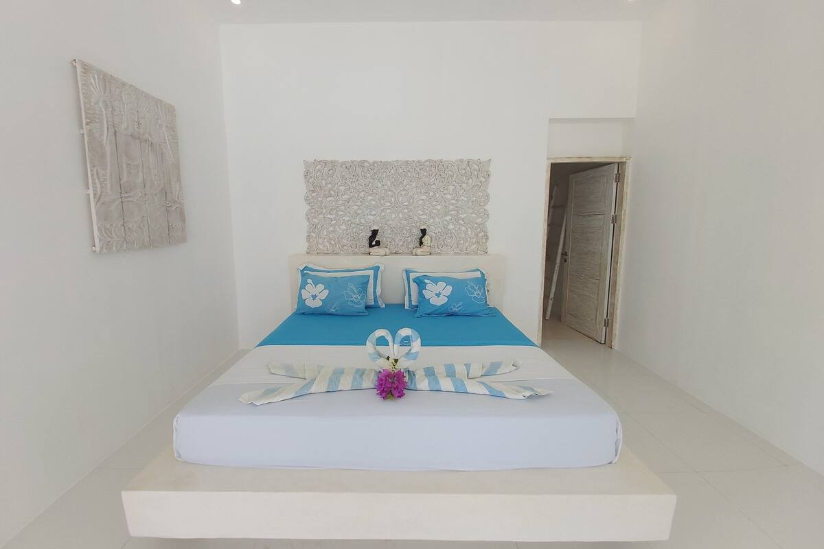 Un dormitorio con cama, almohadas, un muro decorativo y una puerta.