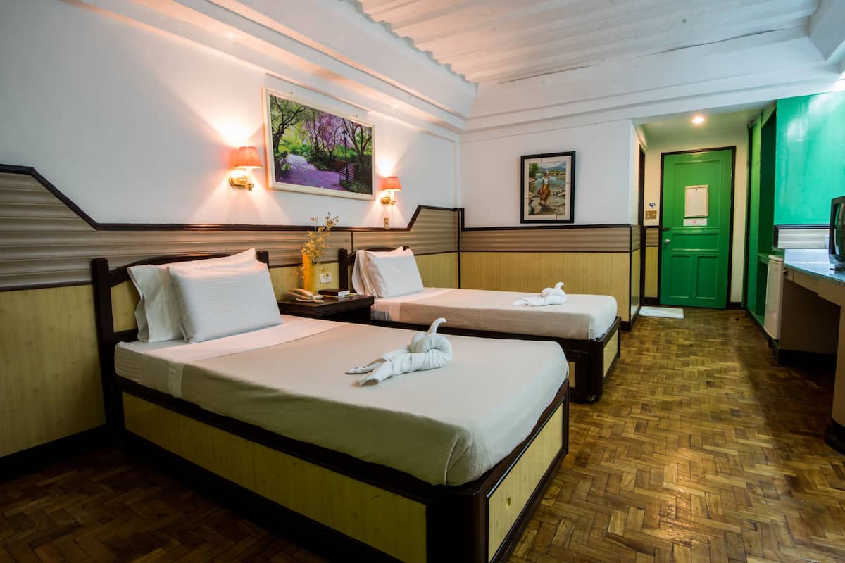 A hotel room with two beds, a wooden herringbone floor, and a green door.