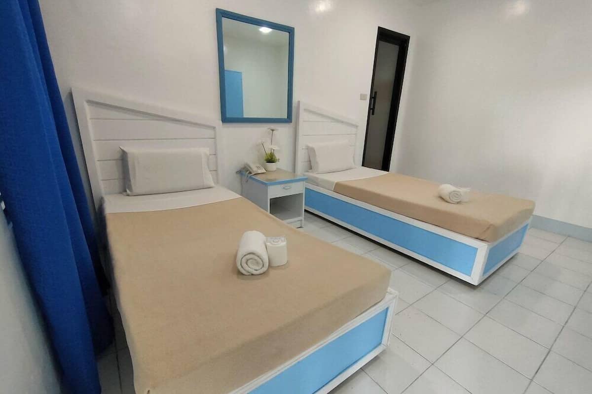 A hotel room with two beds, a nightstand, a mirror, and a door.