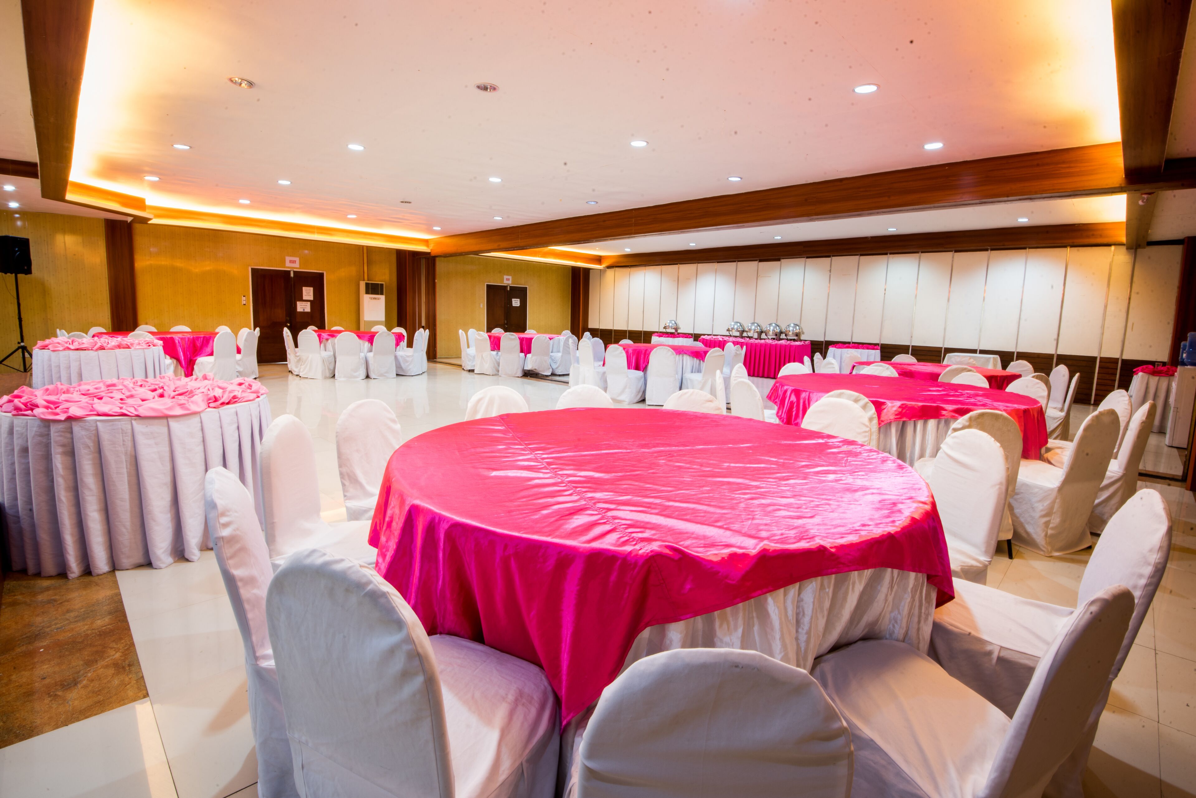 Un salón de banquetes con mesas redondas cubiertas con manteles rosas y sillas blancas.