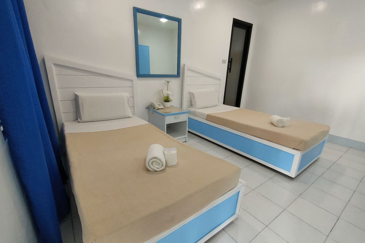 A hotel room with two beds, a small desk with a phone, a mirror, and a door.