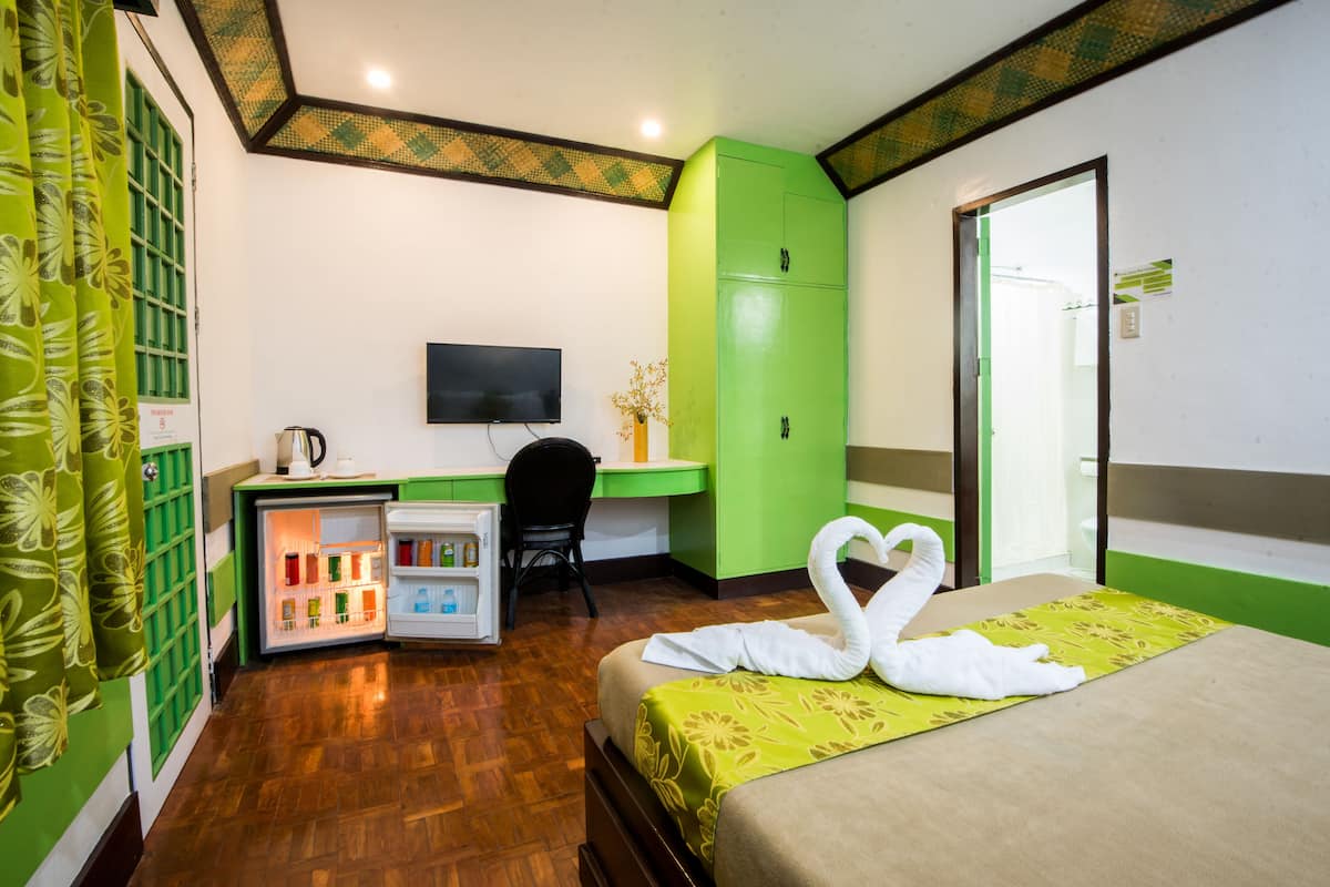 A hotel room with a bed, a desk, a television, a wardrobe, and a minibar.