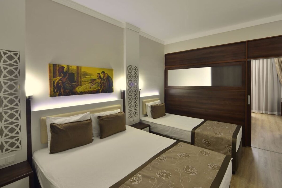 Una habitación de hotel con dos camas, un cuadro grande en la pared, un televisor y un separador decorativo.