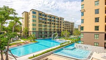 Un hotel moderno con una amplia piscina, varios balcones y exuberante vegetación.