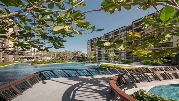 Un hôtel moderne doté d’une piscine centrale, entouré d’une végétation luxuriante et de bâtiments à plusieurs étages.