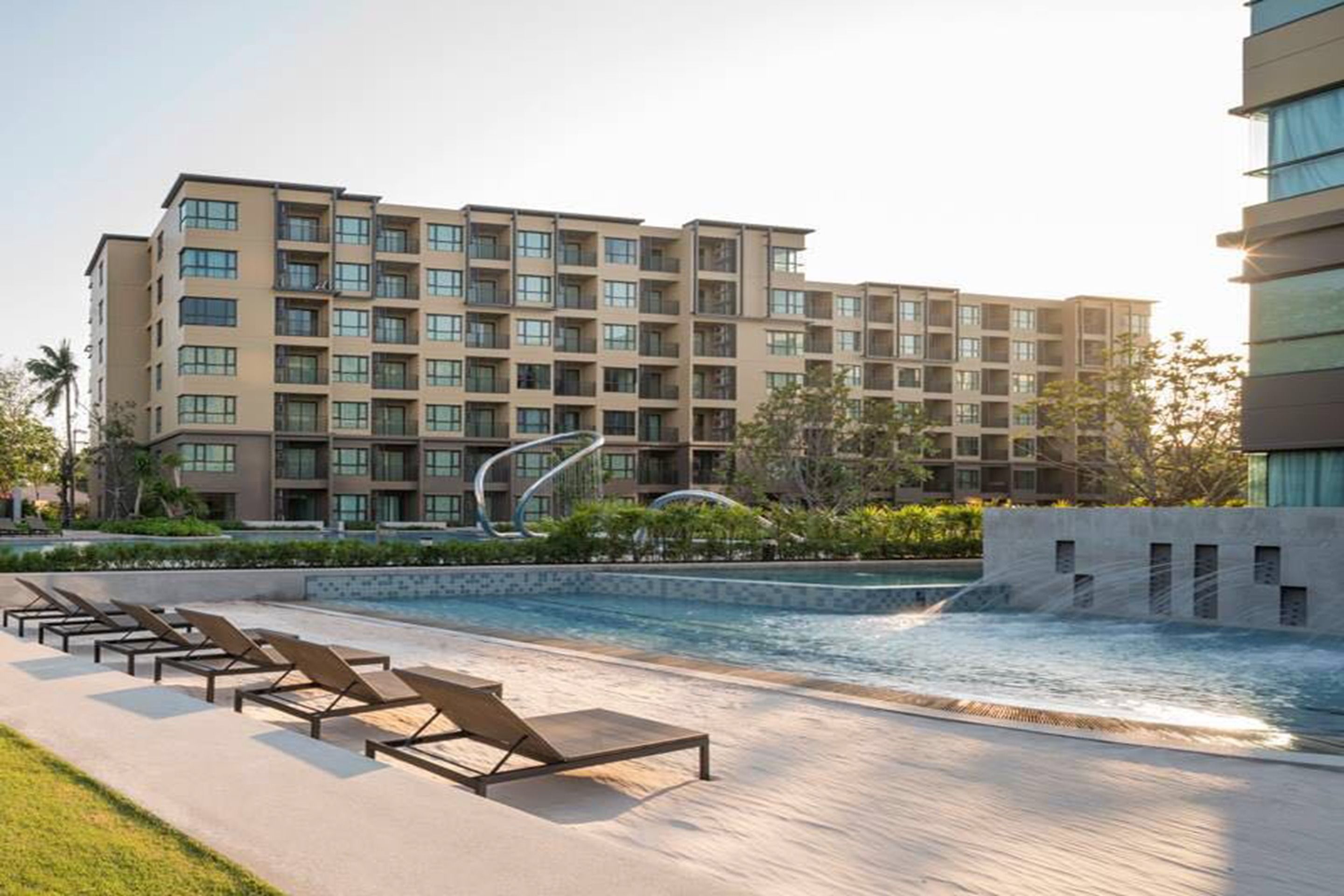 A modern hotel with a swimming pool, sun loungers, and a landscaped garden.