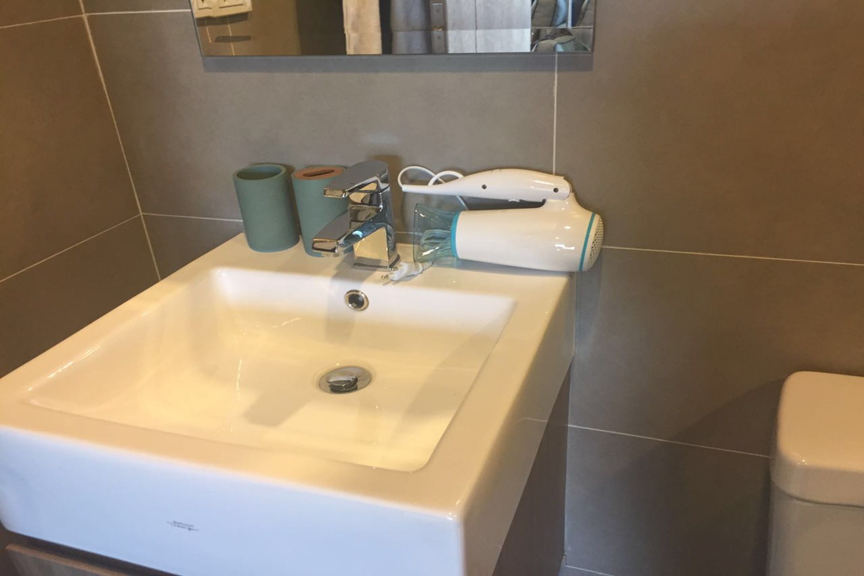 A bathroom sink with a mirror above it, a towel dispenser, and a white handheld showerhead.