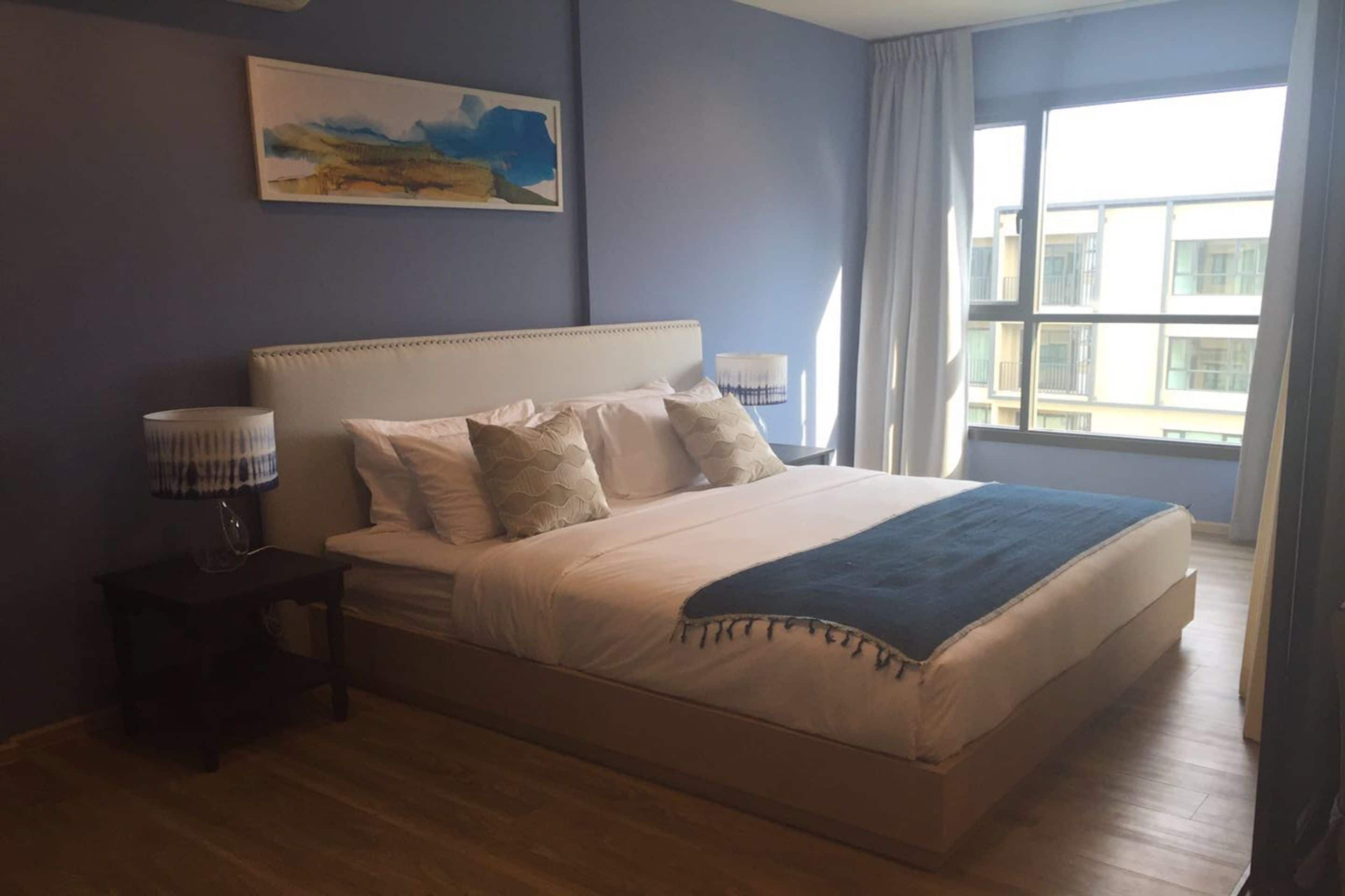 Un dormitorio con una cama grande, una mesita de noche, una lámpara y una ventana con cortinas.