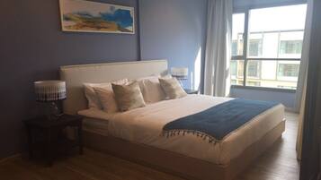 Un dormitorio con una cama grande, una mesita de noche, una lámpara y una ventana con cortinas.