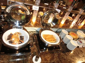 Een buffetopstelling met diverse gerechten en warme pannen, waaronder een bord met 'Sushi'.
