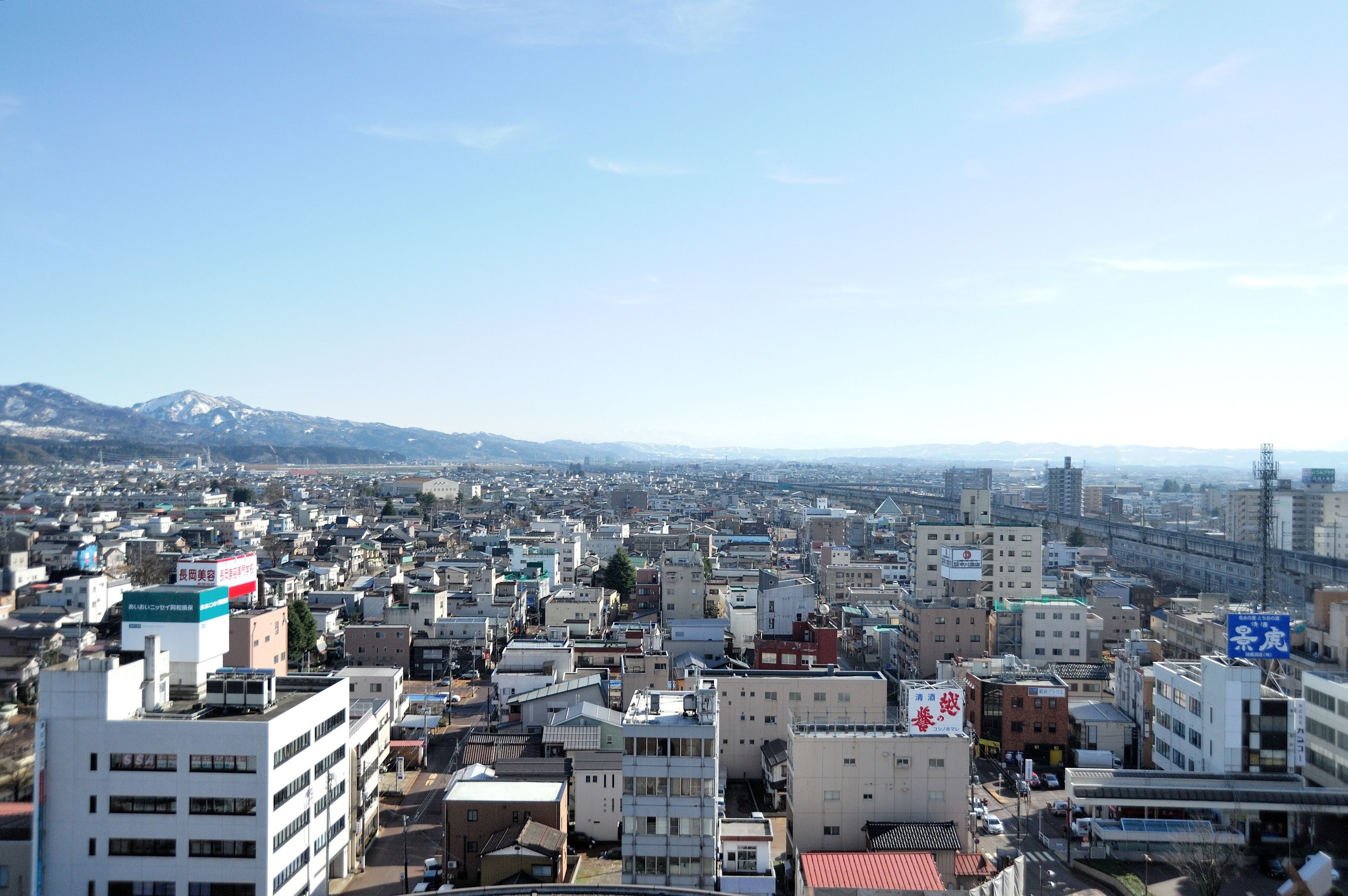 Une zone urbaine densément peuplée, avec de nombreux bâtiments, dont certains arborent des enseignes, et une chaîne de montagnes en arrière-plan.