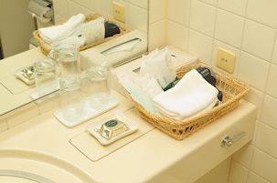 Un baño con inodoro, lavamanos y espejo. Hay artículos de aseo en una cesta y sobre el lavamanos.